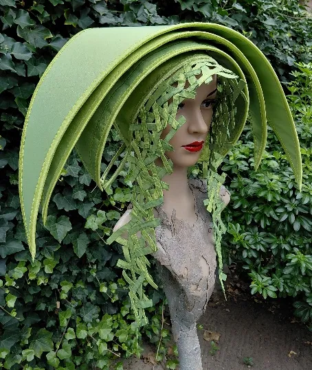 Groen hoedobject met gebogen lagen en fijne bladvormen, op een houten sculptuur