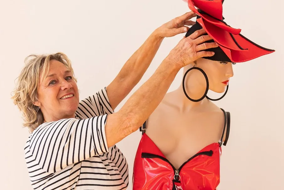 Portret van kunstenaar Jacobine Bekkers terwijl zij een rood hoedobject op een paspop schikt